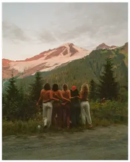 Five friends arm in arm, looking out at a snowy mountain at dusk.