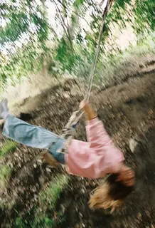 A kid swinging upside down on a rope swing, a blur of motion.