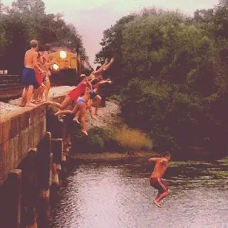 Friends jumping off a bridge into a river.
